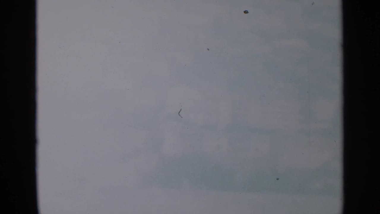 Opening 8mm frame with a mostly pale, low-detail view and visible black film edges before the city view appears.