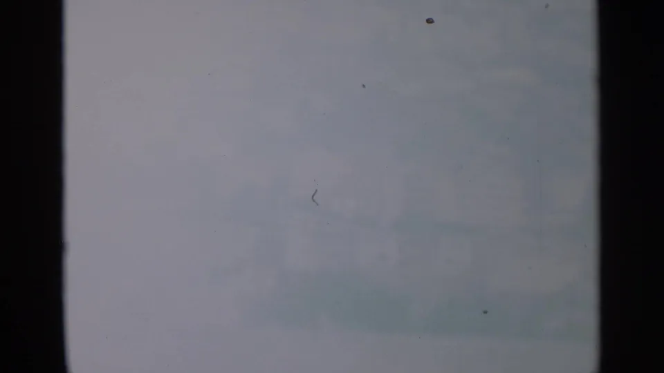 Opening 8mm frame with a mostly pale, low-detail view and visible black film edges before the city view appears.