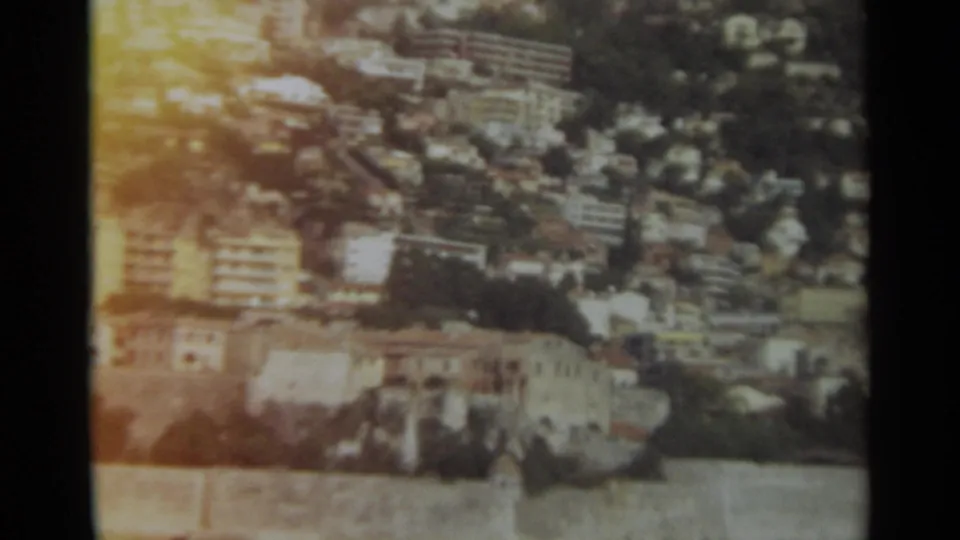 1965 Stockholm 8mm frame showing a soft elevated view of dense hillside buildings, roads, and trees.
