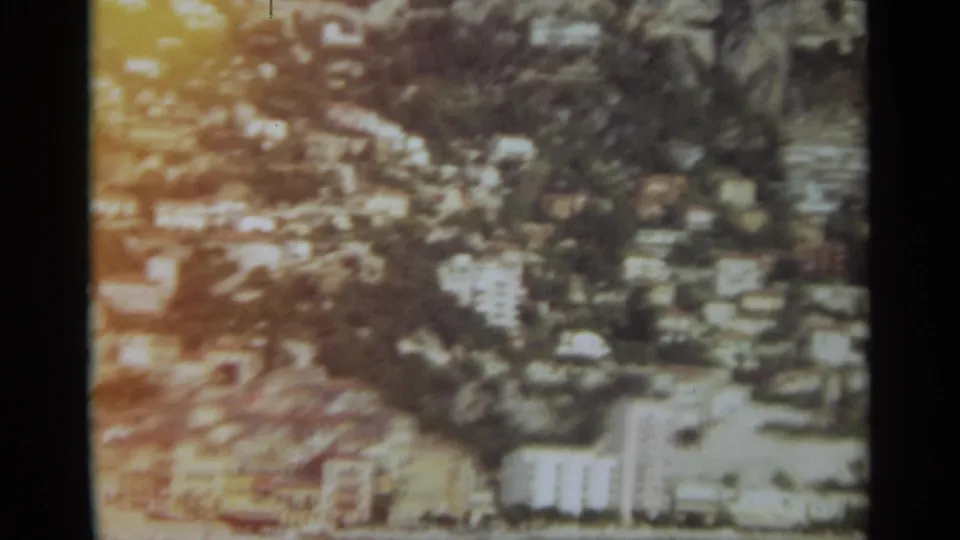 1965 Stockholm 8mm frame showing a blurred elevated cityscape with hillside housing, trees, and light apartment blocks.