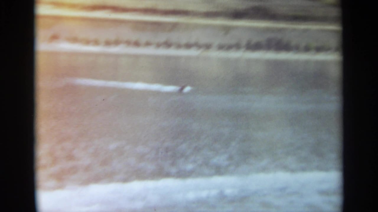 Distant boat wake on open water with shoreline in the background.