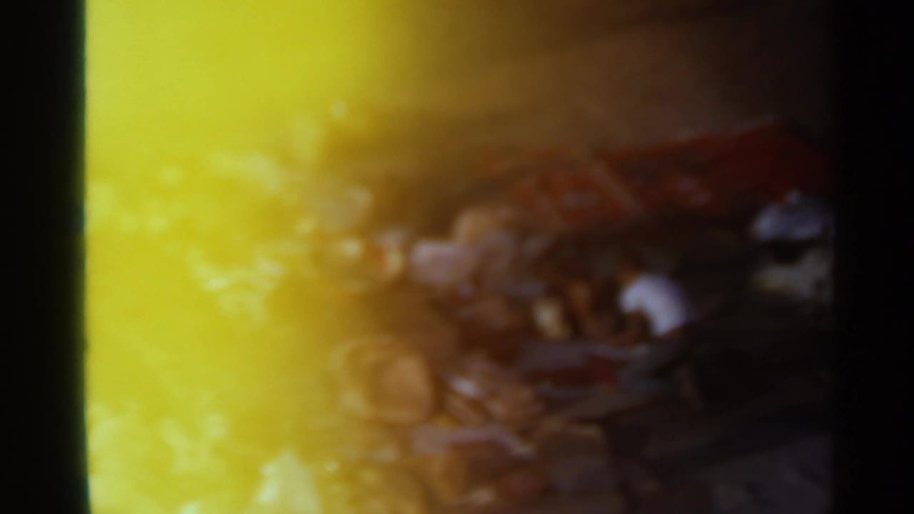 1965 Tangier street-market view partly obscured by yellow sun flare, with shadowed people and scattered goods barely visible.