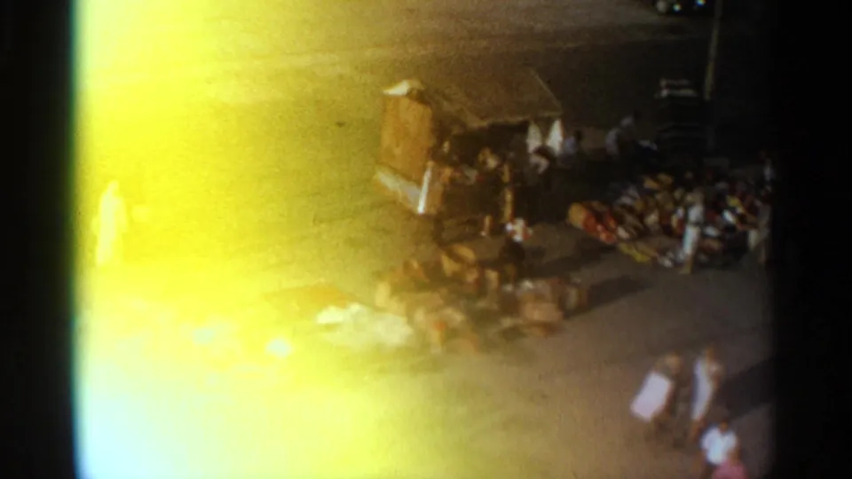 1965 Tangier market scene with a cart or stall, goods laid out on the pavement, and pedestrians crossing through strong yellow flare.