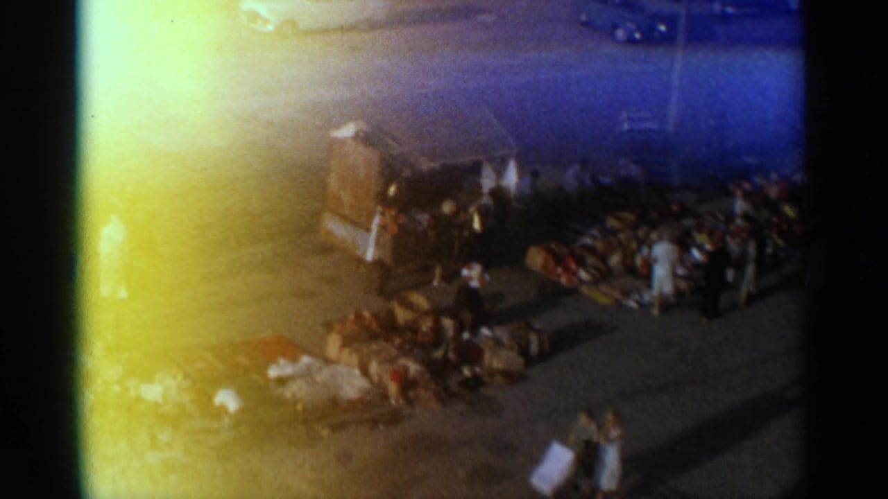 Elevated view of market activity with people beside a kiosk and goods on the ground.