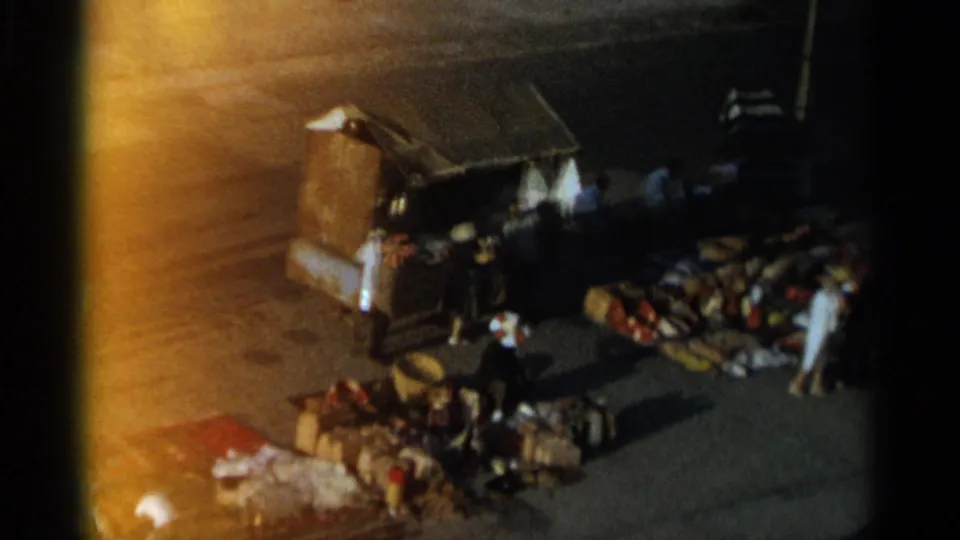 1965 Tangier market activity from above, with people gathered by a kiosk and goods spread on the ground.