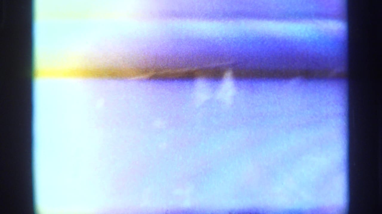 Soft, overexposed 8mm frame from the Tangier market clip, dominated by pale blue-purple light and dark film borders.
