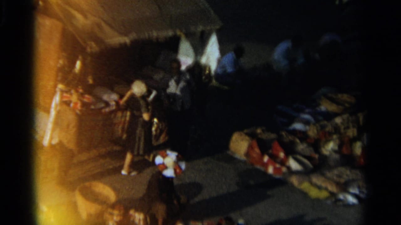 Tangier, Morocco night market scene in 1965, with people near ground-laid goods beneath a canopy and warm artificial lighting.