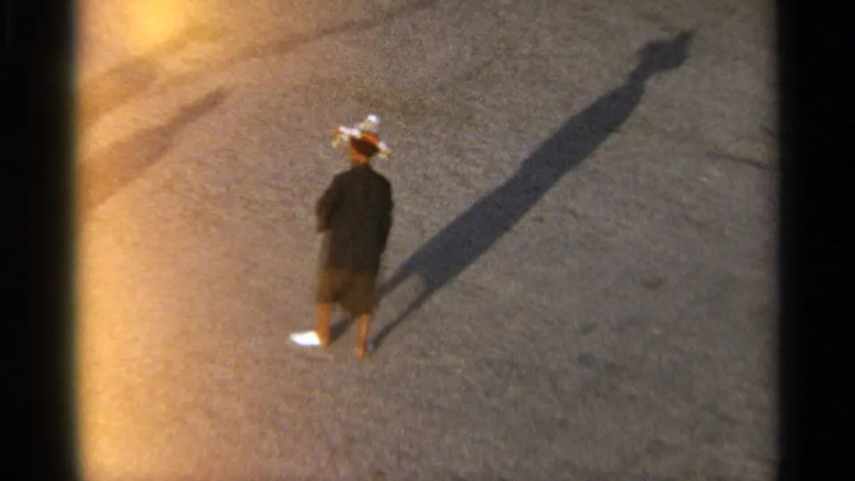 Tangier, Morocco 1965 frame of a lone pedestrian in dark clothing and a light hat crossing open pavement with a long afternoon shadow.