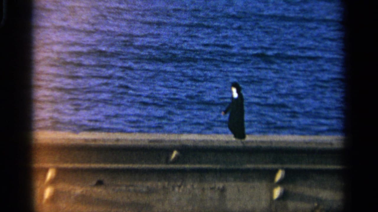 Distant person in dark clothing walking beside a large body of water.
