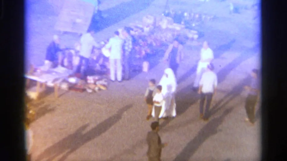 The final frame shifts to a soft, distant view of several people on a paved waterfront area in the same Tangier home movie.