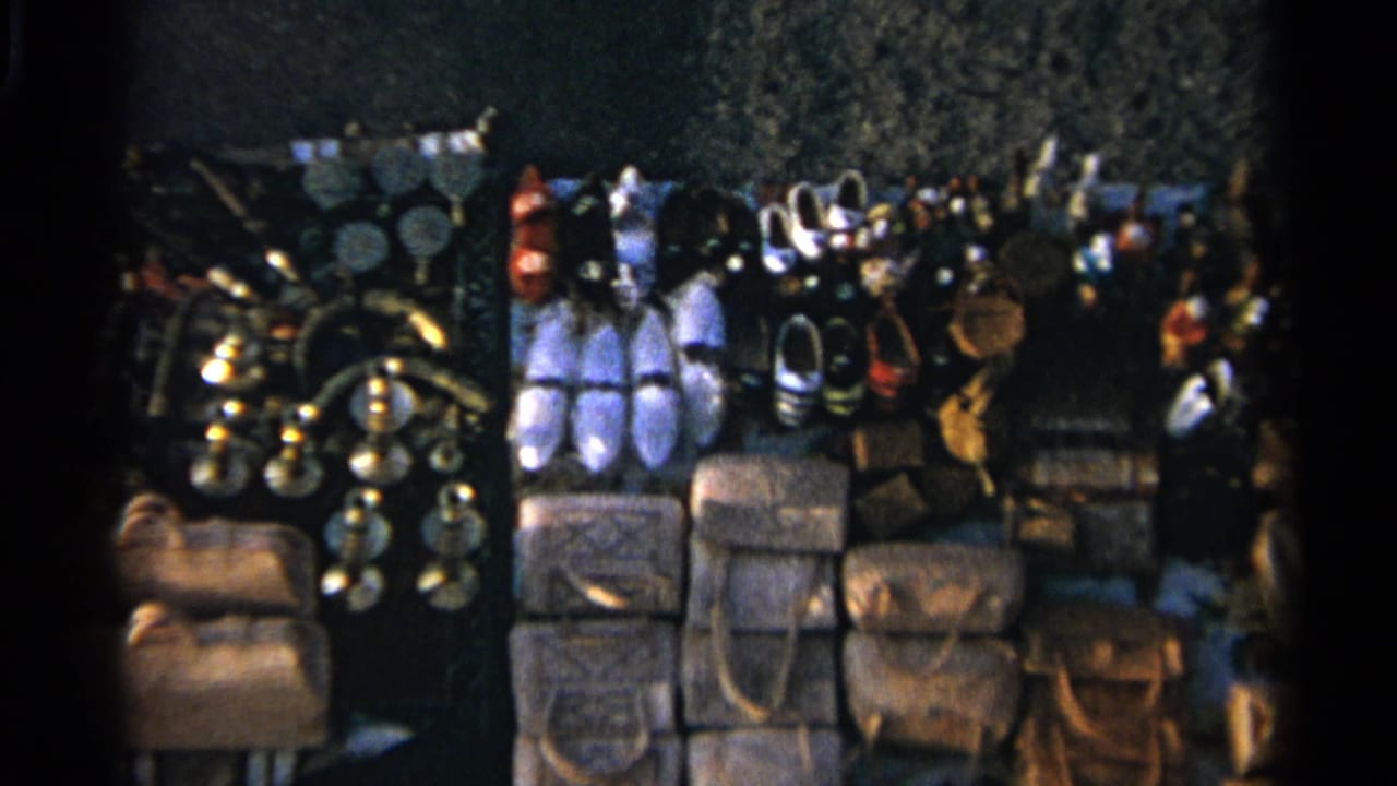 Dense stall display with slippers, handbags, metal objects and hanging craft items.