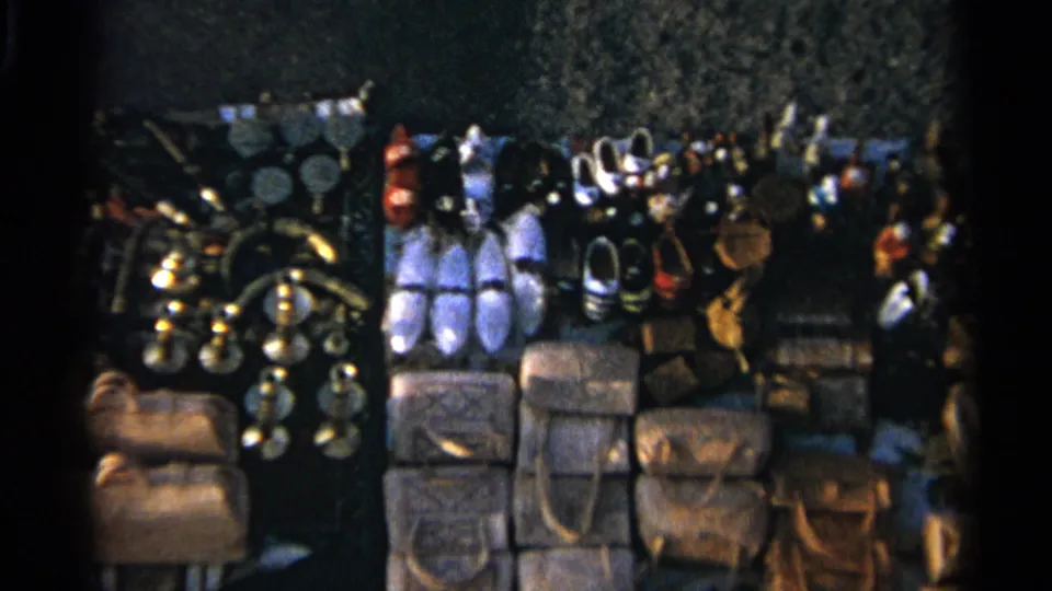 Handheld 8mm view of a Tangier market display showing slippers, leather bags, metalware and small hanging goods.