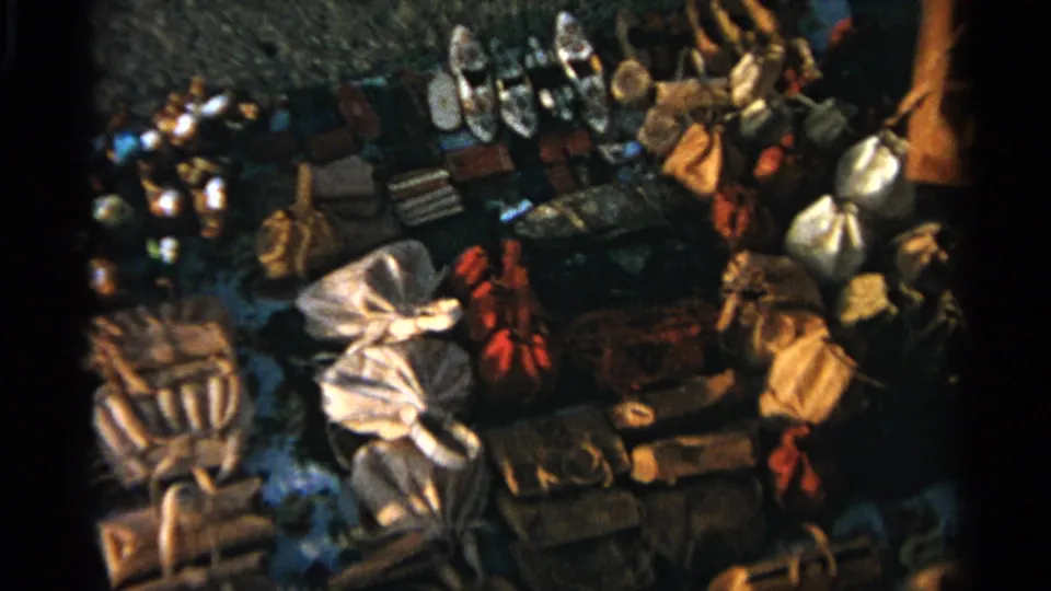 1965 Tangier home-movie frame showing an outdoor market display with shoes, bags, textiles, and bundled goods seen from above.