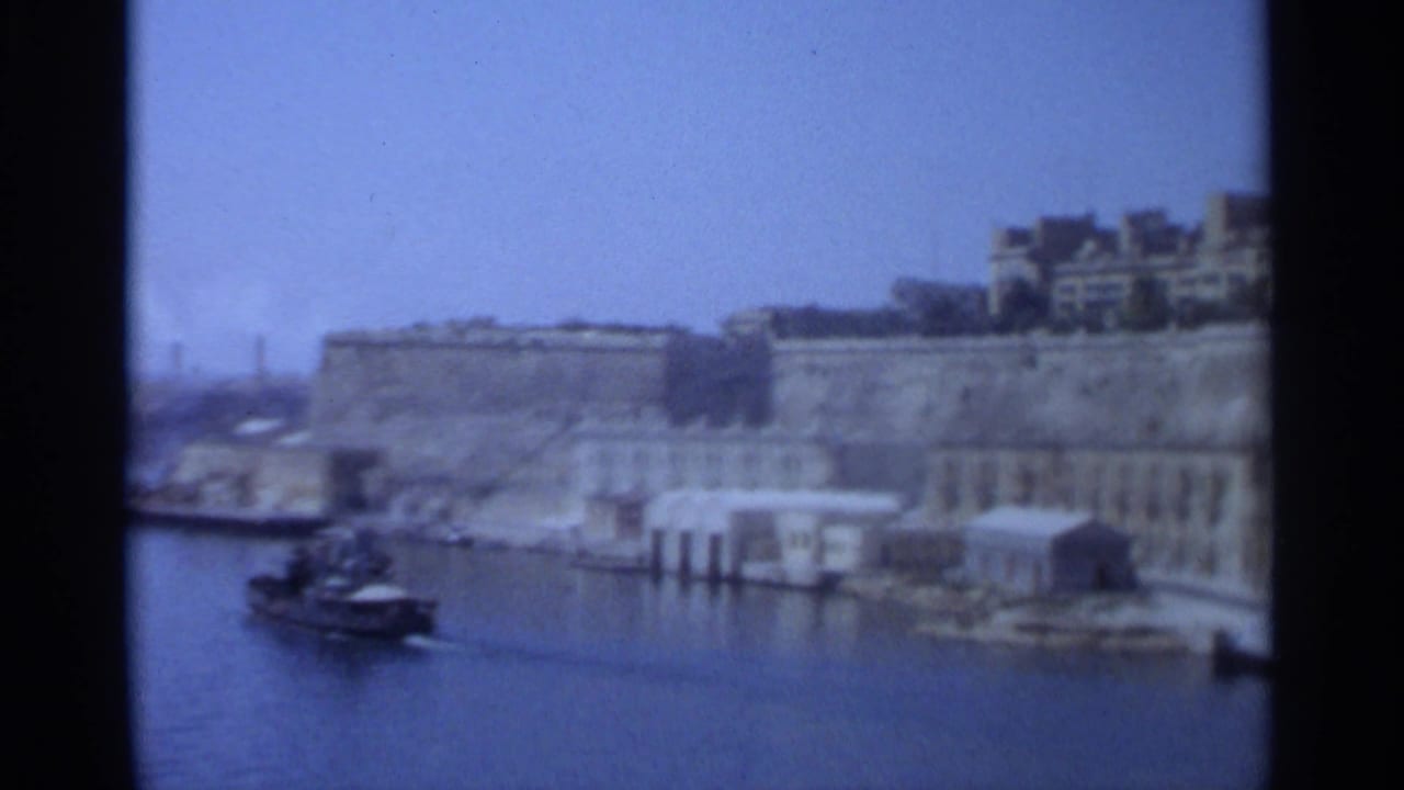 Tangier, Morocco, 1965 home-movie frame showing the harbor waterfront, stone walls, waterside buildings, and a small boat.