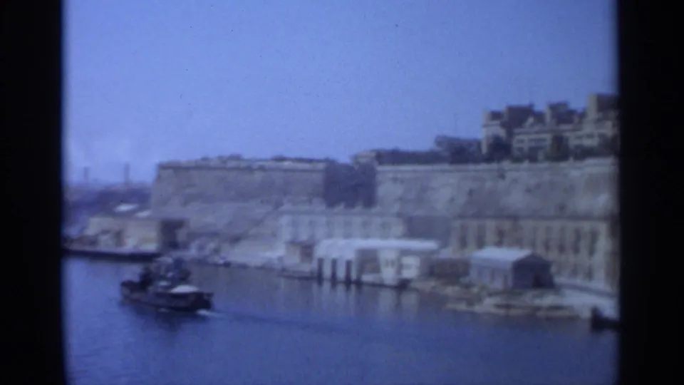 Tangier, Morocco, 1965 home-movie frame showing the harbor waterfront, stone walls, waterside buildings, and a small boat.