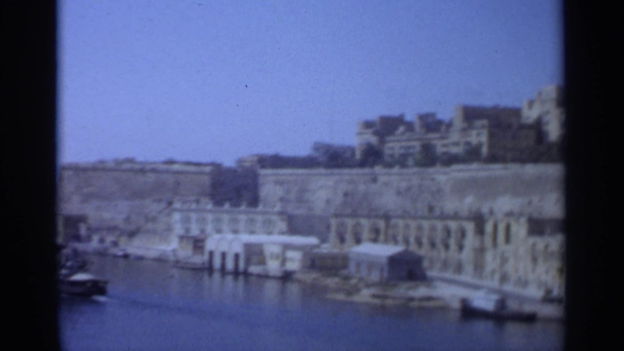 1965 Tangier harbor view with stone quay buildings, calm water, small boats, and dark 8mm frame borders.