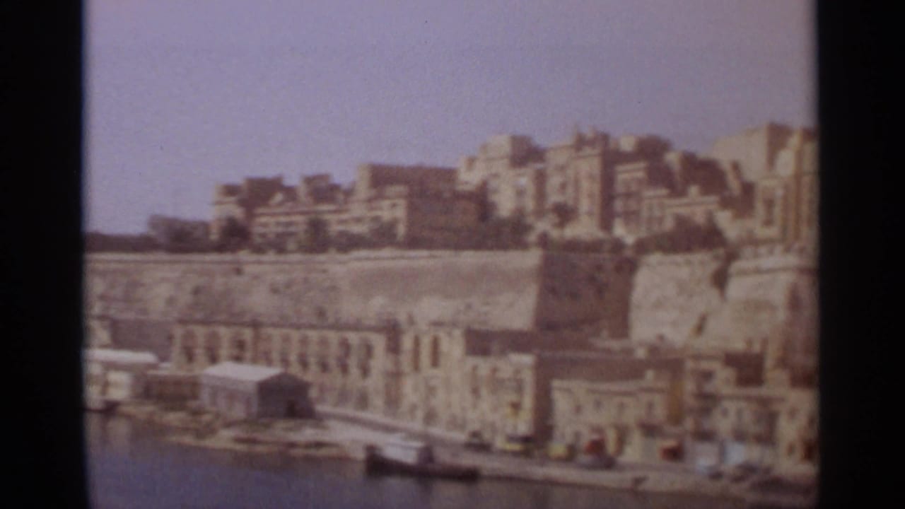 Tangier waterfront in 1965, showing stone harbor structures, moored boats, hillside buildings, and faded 8mm color.