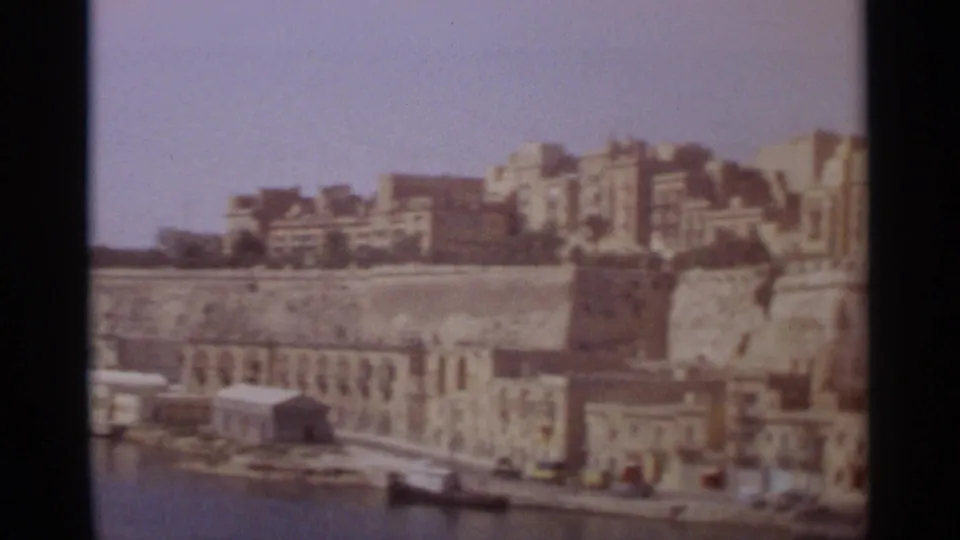 Tangier waterfront in 1965, showing stone harbor structures, moored boats, hillside buildings, and faded 8mm color.