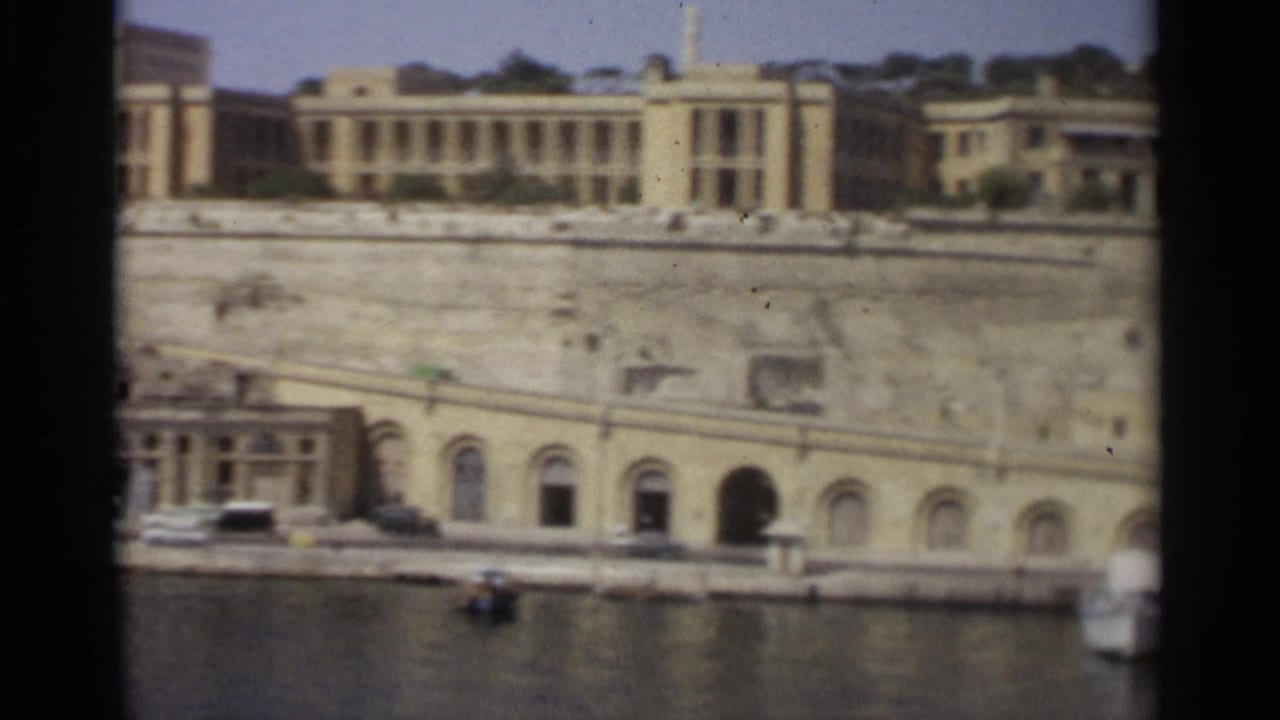 Tangier harborfront in 1965, showing a broad stone wall, arched openings, waterfront road, and pale buildings above the quay.
