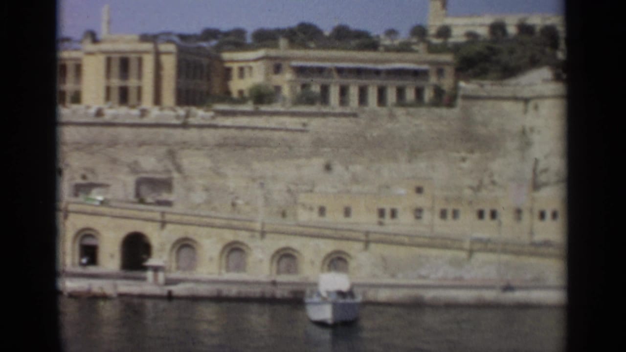 1965 Tangier waterfront with an arched doorway in the stone embankment, parked vehicles, and a small boat near the quay.