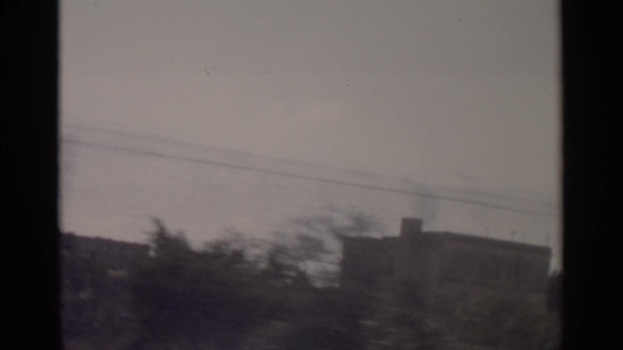 Tangier waterfront cutaway with dark shoreline forms, trees, a building silhouette, and overhead lines in faded 8mm exposure.