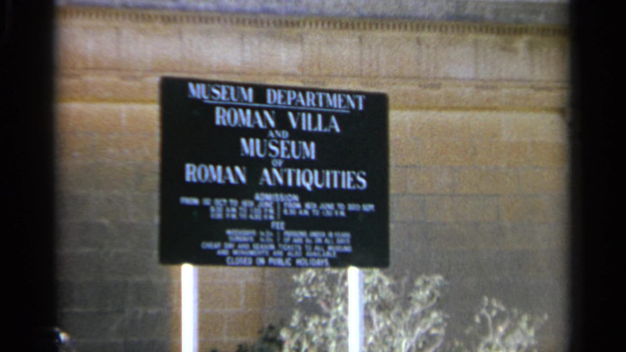 Close visitor-shot view of the Roman Villa and Museum of Roman Antiquities sign in Tangier, Morocco, with 8mm softness and grain.