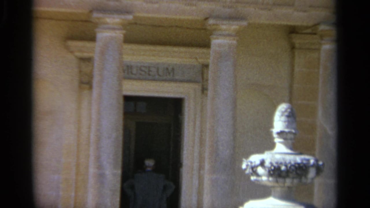 The final Tangier frame keeps the man near the dark entrance, with the museum sign, columns, and sunlit fountain or urn still visible.
