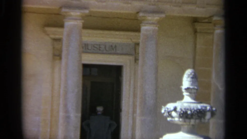 The final Tangier frame keeps the man near the dark entrance, with the museum sign, columns, and sunlit fountain or urn still visible.