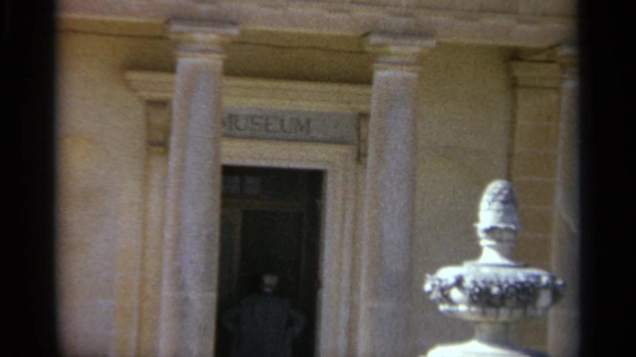 1965 Tangier 8mm frame showing a museum entrance with stone columns, a carved sign, white urn sculpture, and a silhouetted doorway figure.