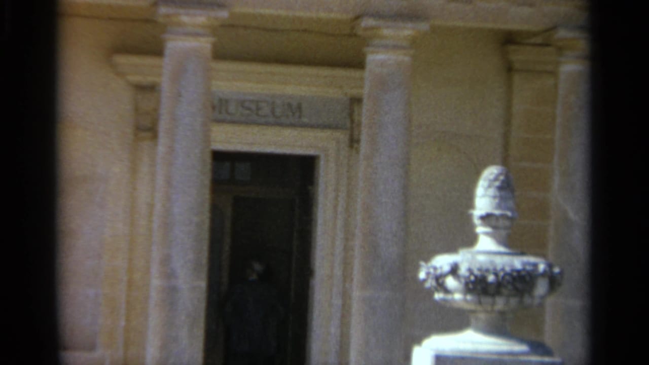 1965 Tangier 8mm view of a museum entrance, with classical columns, a foreground white urn sculpture, and a dark-clothed figure in the doorway.