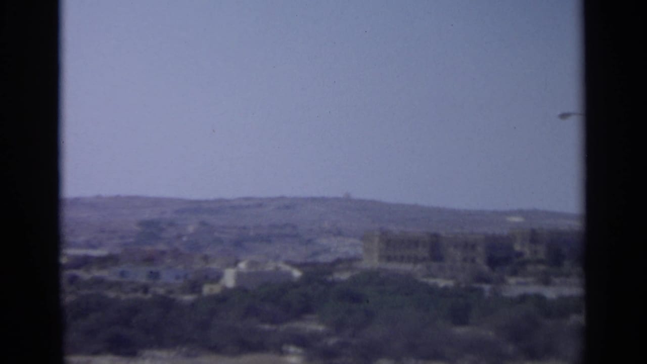 1965 Tangier view with a central window divider framing hazy hills and low urban buildings in the distance.
