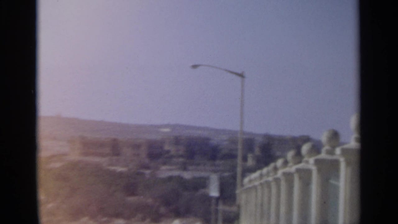 1965 Tangier frame showing a hazy city view beyond a streetlight and white balustrade with round finials.
