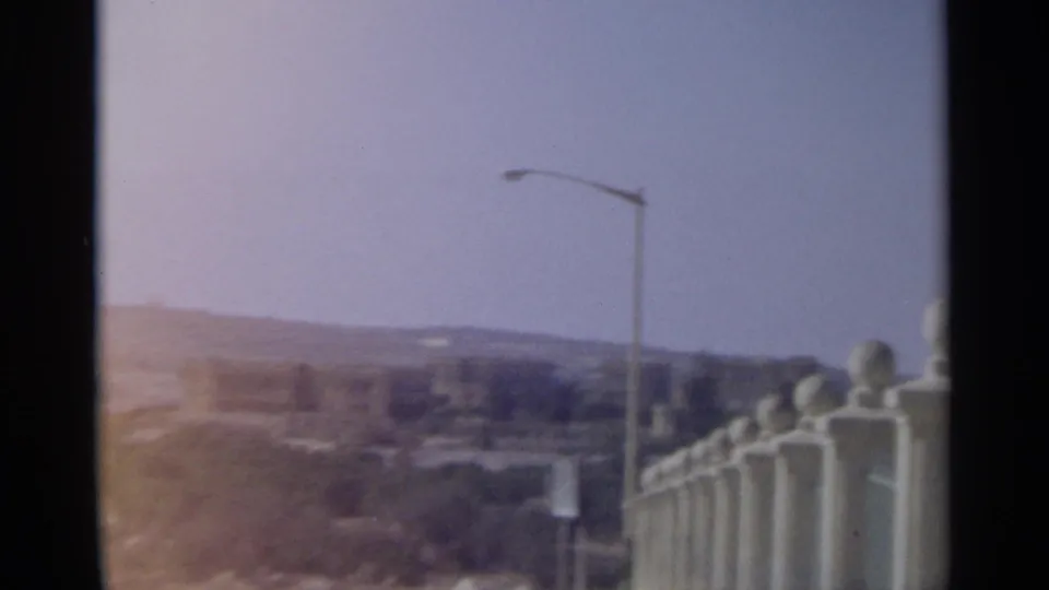 1965 Tangier frame showing a hazy city view beyond a streetlight and white balustrade with round finials.