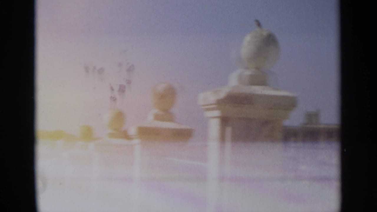 1965 Tangier home-movie frame with warm flare across white balustrade finials and a distant hillside skyline.