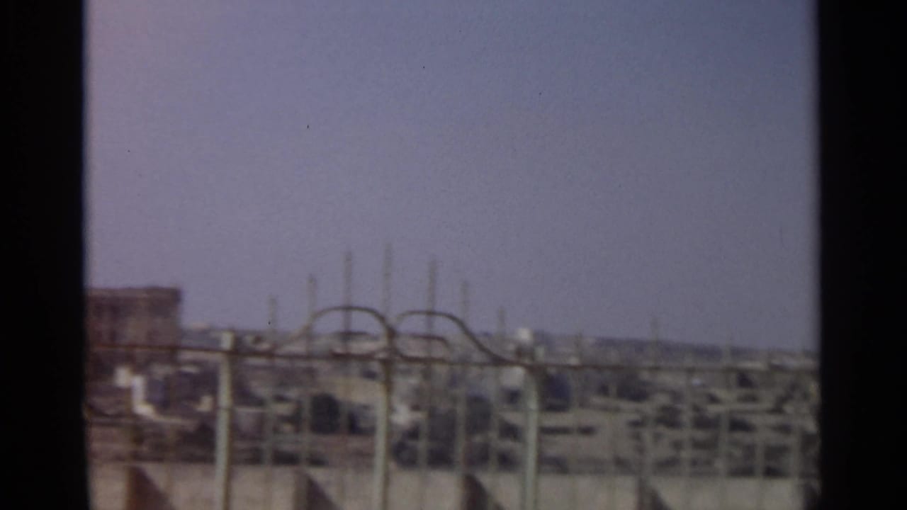 1965 Tangier rooftop view with metal fence lines in the foreground and distant urban buildings softened by 8mm grain.