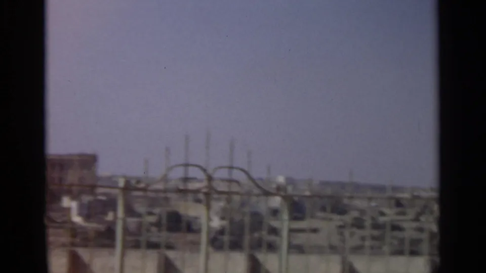 1965 Tangier rooftop view with metal fence lines in the foreground and distant urban buildings softened by 8mm grain.