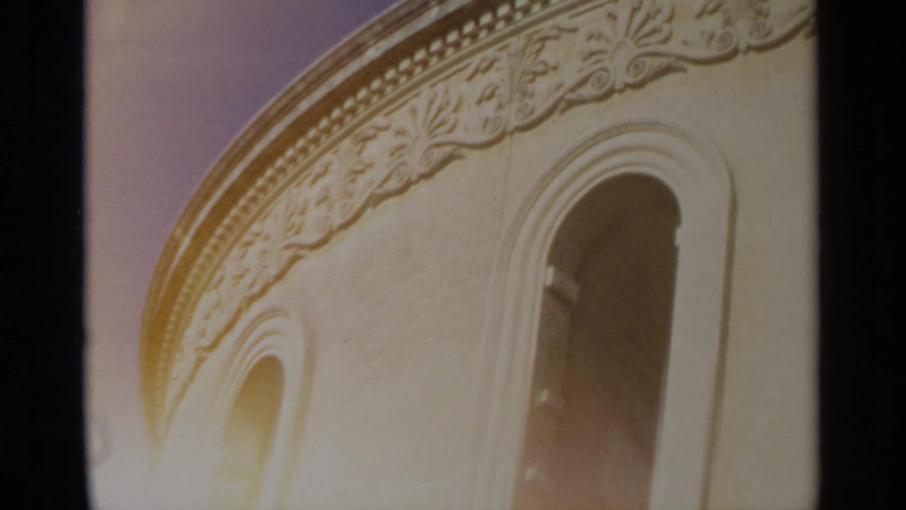 1965 Tangier home-movie frame of an ornate pale facade, arched window forms, carved trim, and bright exposure bloom.