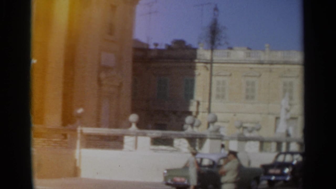 1965 Tangier 8mm frame with a pale building facade, balustrade, parked cars, and a person near the lower right.