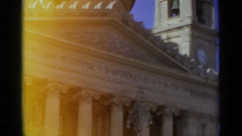 1965 Tangier home-movie frame showing a classical building facade with columns, roofline detail, and a partial clock tower under warm flare.