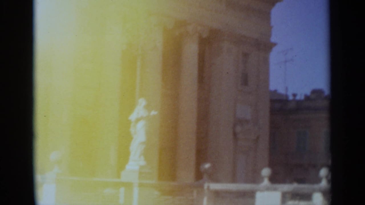 1965 Tangier home-movie frame showing bright tan columns, a white statue, railings, and distant building facades under blue sky.