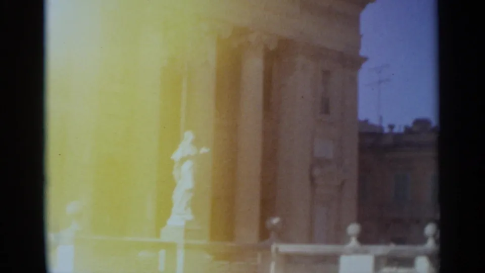 1965 Tangier home-movie frame showing bright tan columns, a white statue, railings, and distant building facades under blue sky.