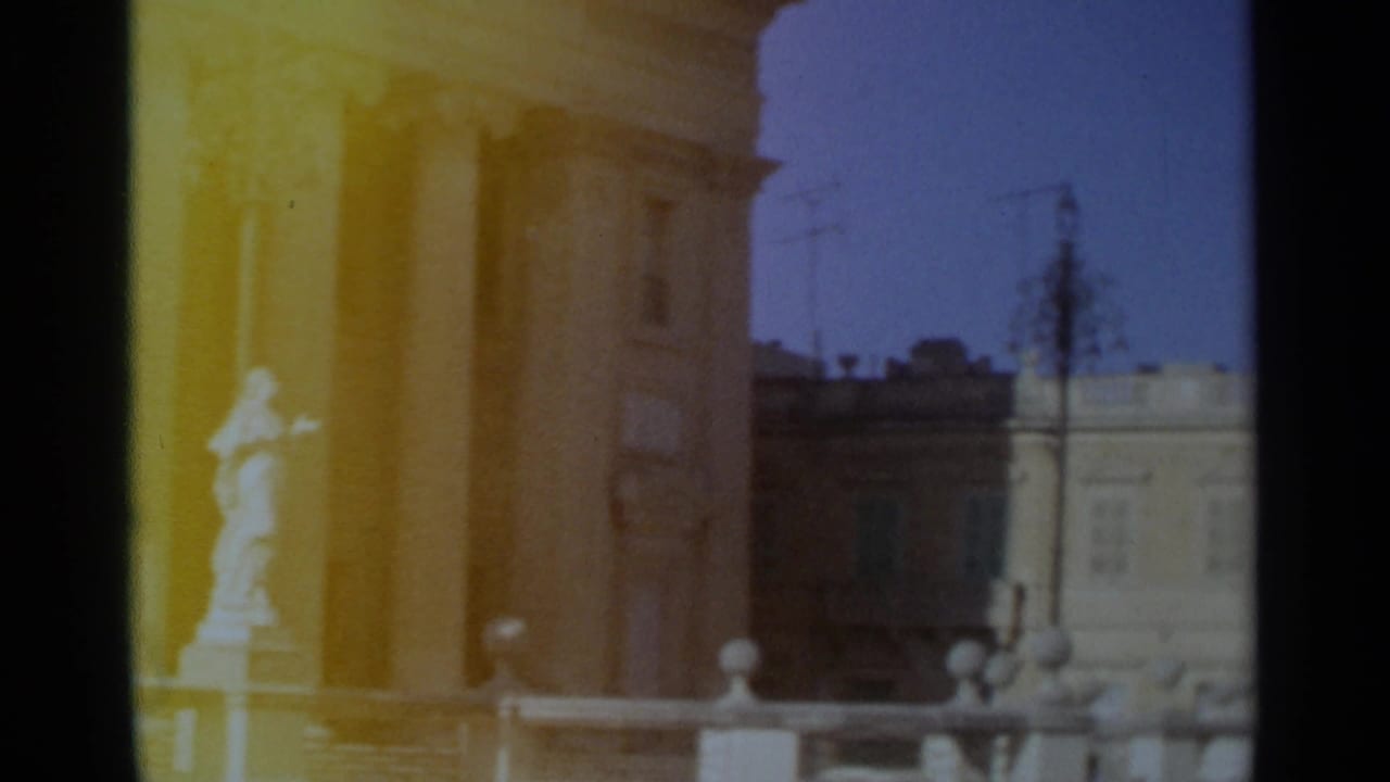 1965 Tangier frame with a pale statue set against columns, tan masonry, street lamps, and a light building across the street.