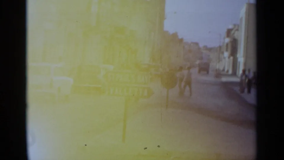 1960s 8mm street view with pedestrians near cars and a directional sign, with strong yellow color cast and soft exposure.