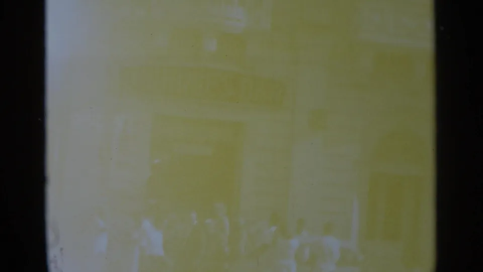 Very faded 8mm street view with several people near a building frontage, softened by overexposure and yellow color shift.