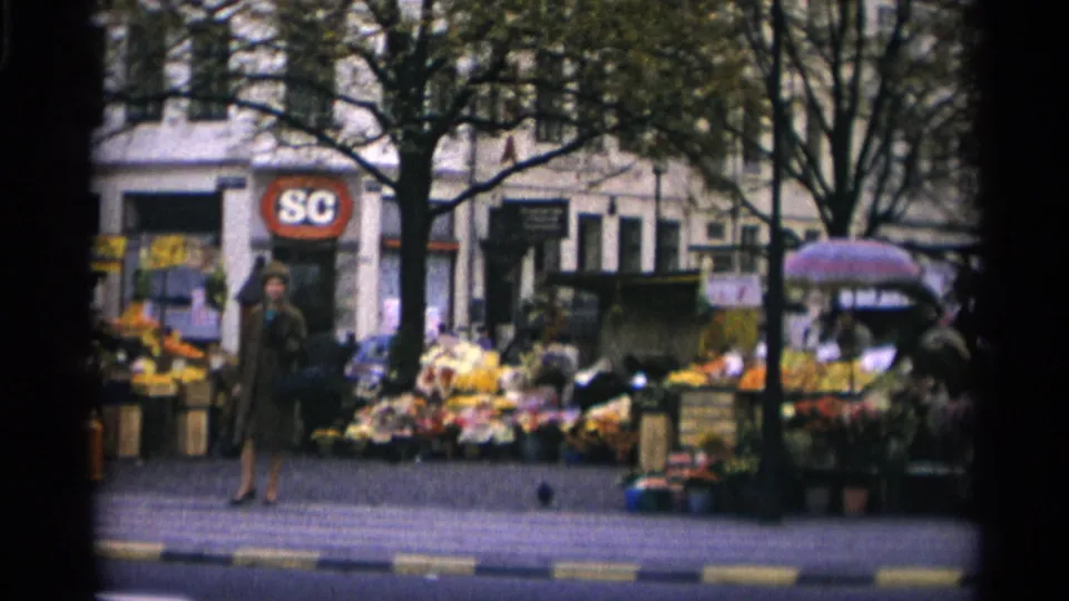 1966 Copenhagen street flower market seen from across the road, with stalls, pedestrians, trees, and an SC sign behind the displays.