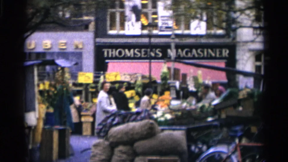 Copenhagen market scene with flower stalls, people, a handcart in the foreground, and a readable Thomsens Magasiner storefront sign.