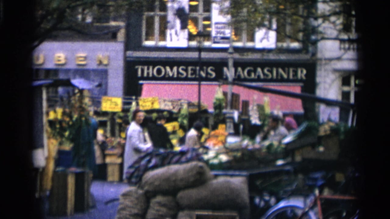 Outdoor produce market with shoppers, stalls, sacks, bicycles, and a THOMSENS MAGASINER storefront.