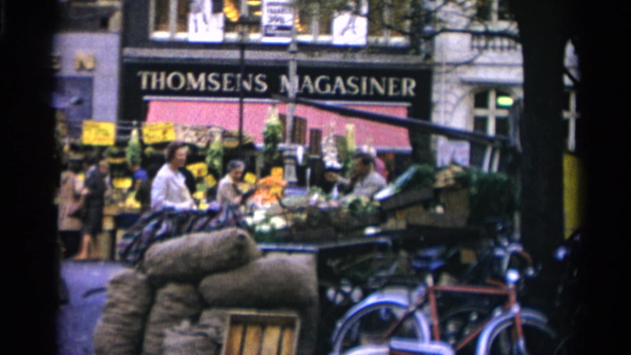 Market stalls with shoppers and vendors in front of a THOMSENS MAGASINER storefront and parked bicycles.