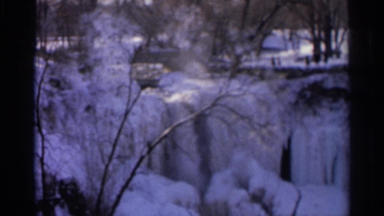 1966 Hamel, Minnesota 8mm frame showing a frozen waterfall, snowy banks, bare winter trees, and small distant figures near the water.