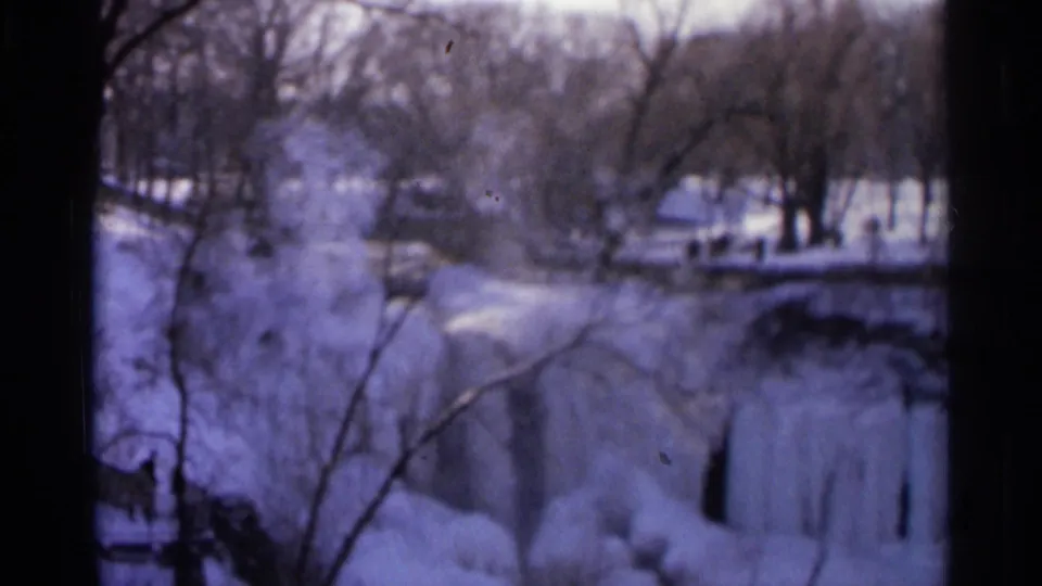 Vintage 8mm frame from Hamel, Minnesota showing a soft, purple-blue winter view of frozen falls and snowy banks.
